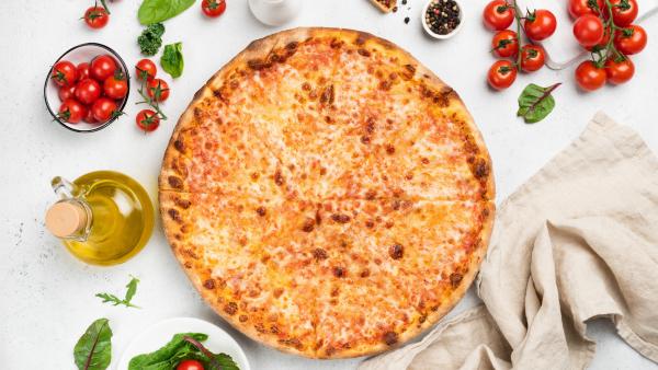 Cheese pizza from above surrounded by tomatoes, oil and basil