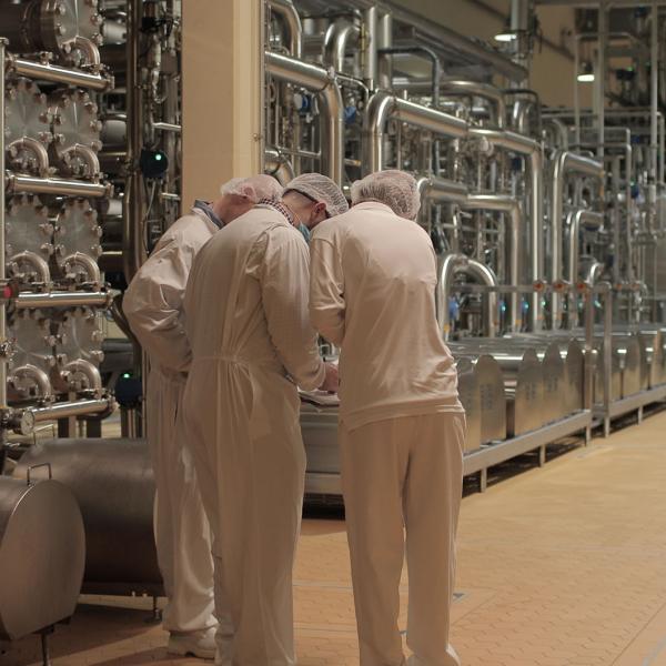 Three employees in white overalls working in a Glanbia Ireland factory discussing quality