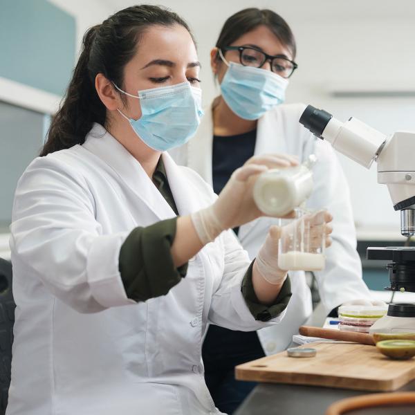 A Glanbia Ireland scientist pouring milk from a bottle to a beaker in a lab