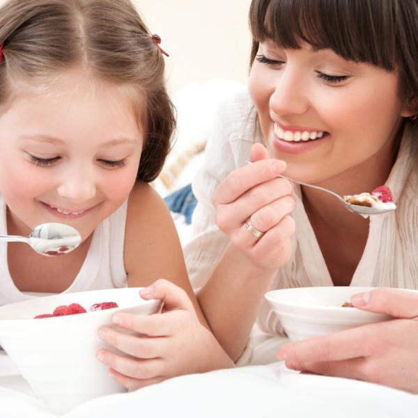 Static image of a mother and daughter smiling and eating yoghurt. 