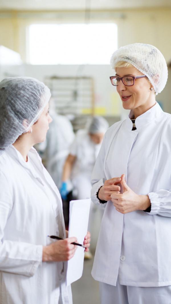 Two women in a factory discussing ingredients