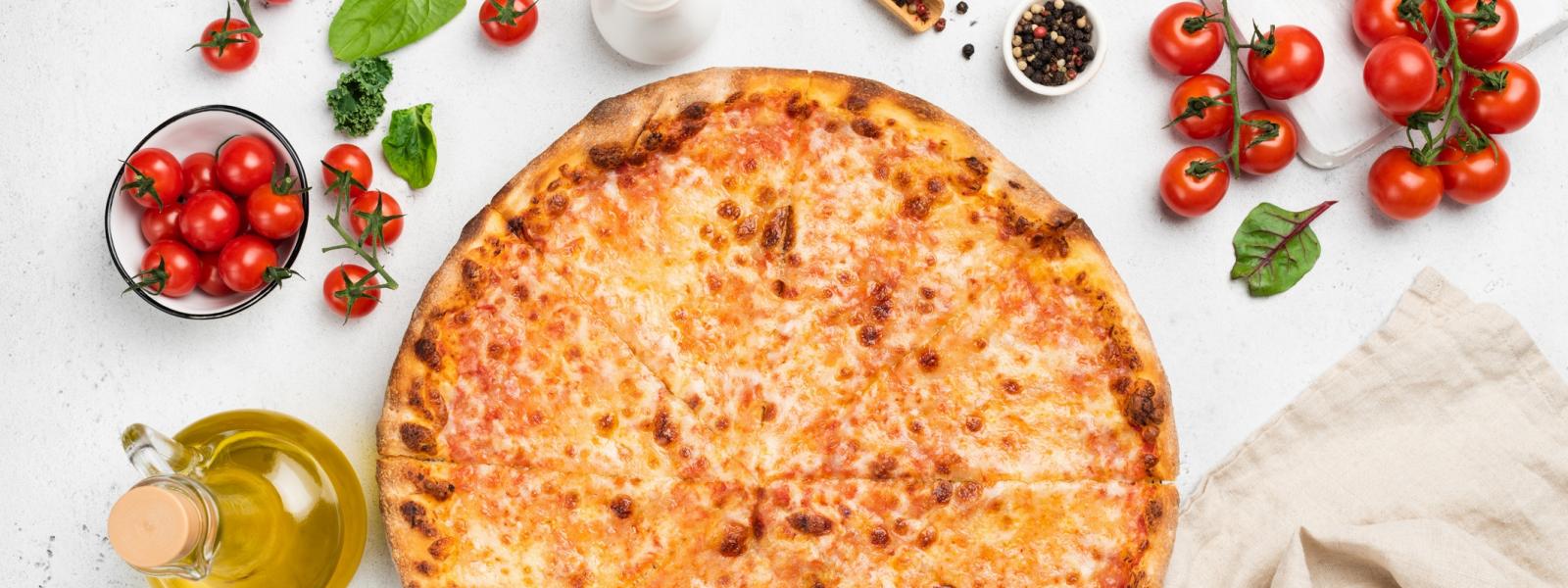 Cheese pizza from above surrounded by tomatoes, oil and basil