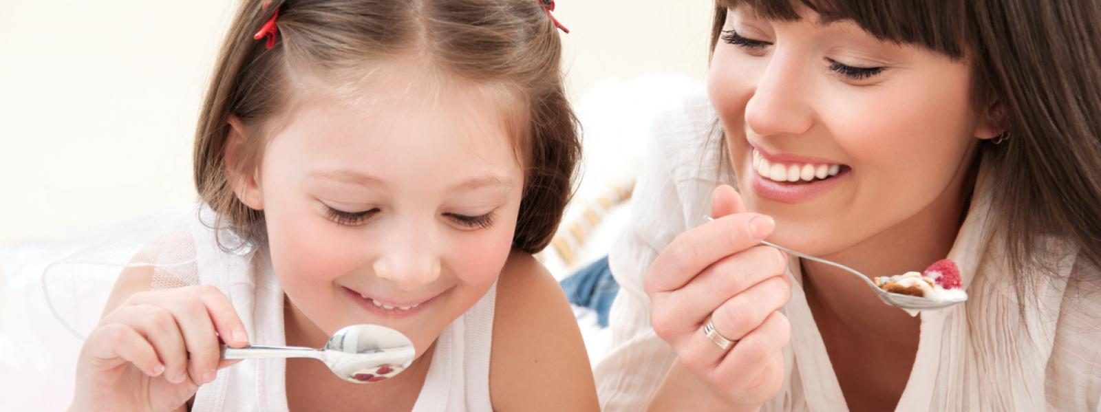 Static image of a mother and daughter smiling and eating yoghurt. 
